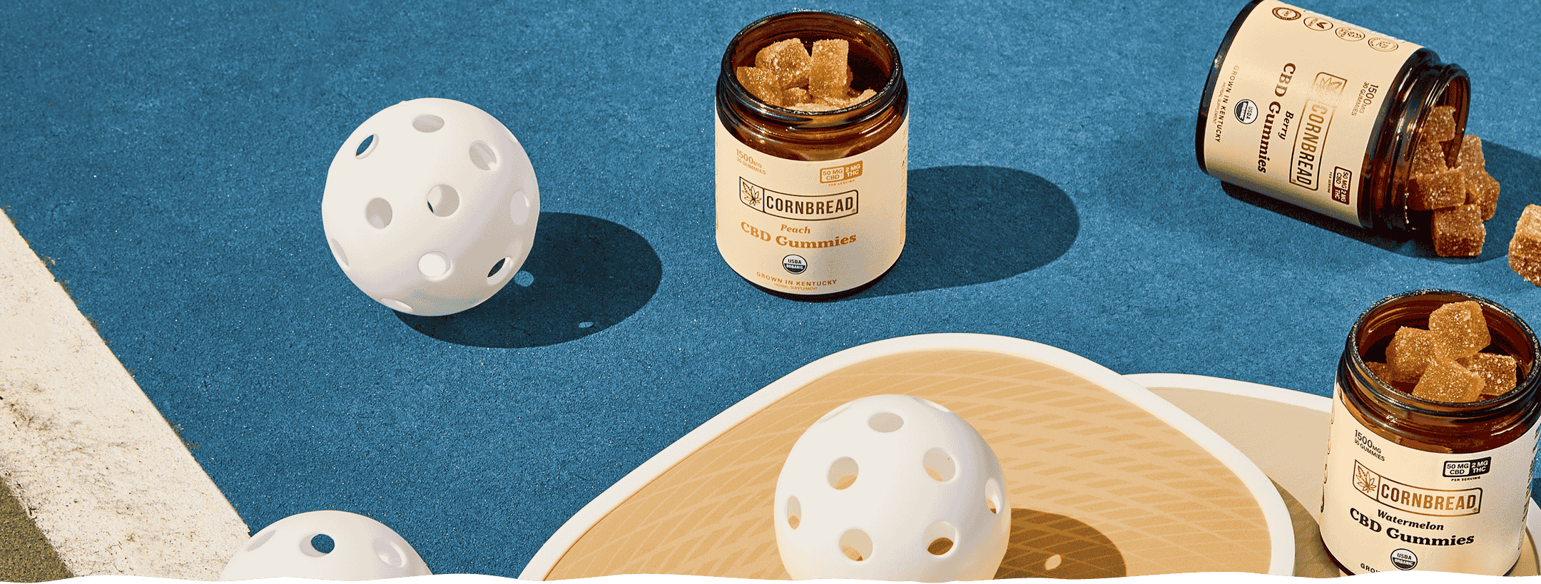 Three jars of Cornbread's full spectrum CBD gummies on a pickleball court