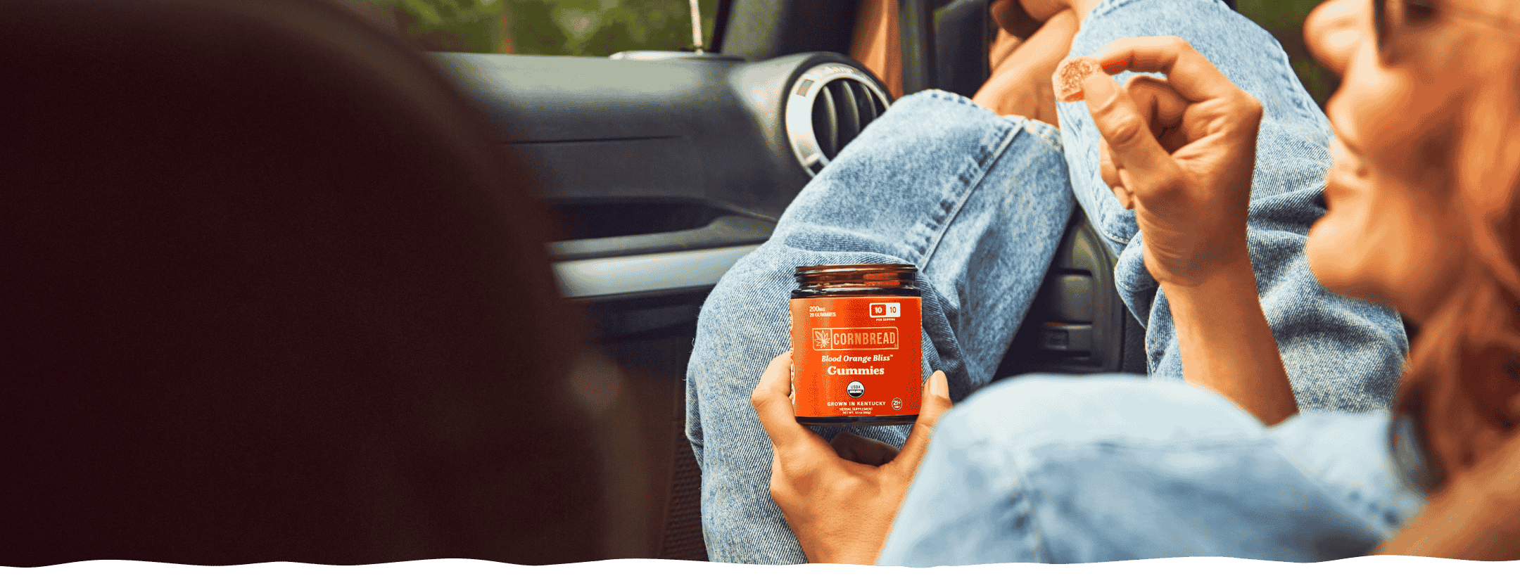 A woman laughing in the passenger seat with a Cornbread Hemp Blood Orange Bliss THC Gummy