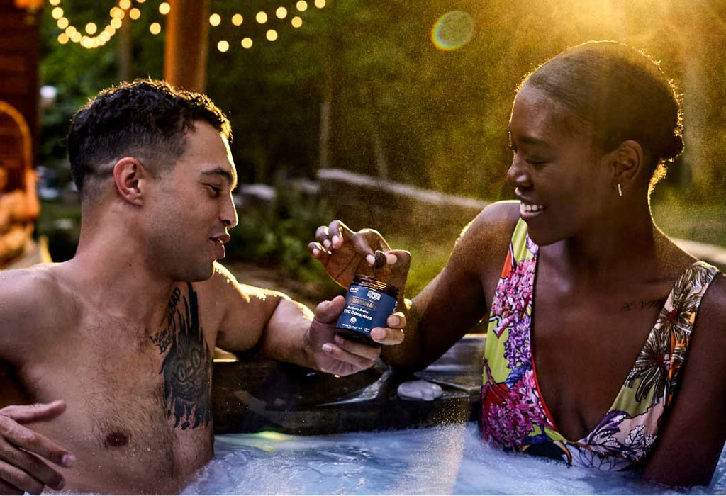Two people enjoy Cornbread Hemp THC gummies in a hot tub.